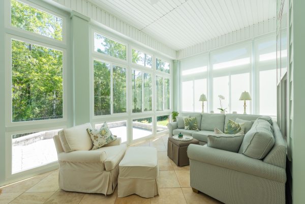 A beautiful sunroom installed by sunroom contractors with white furniture inside.