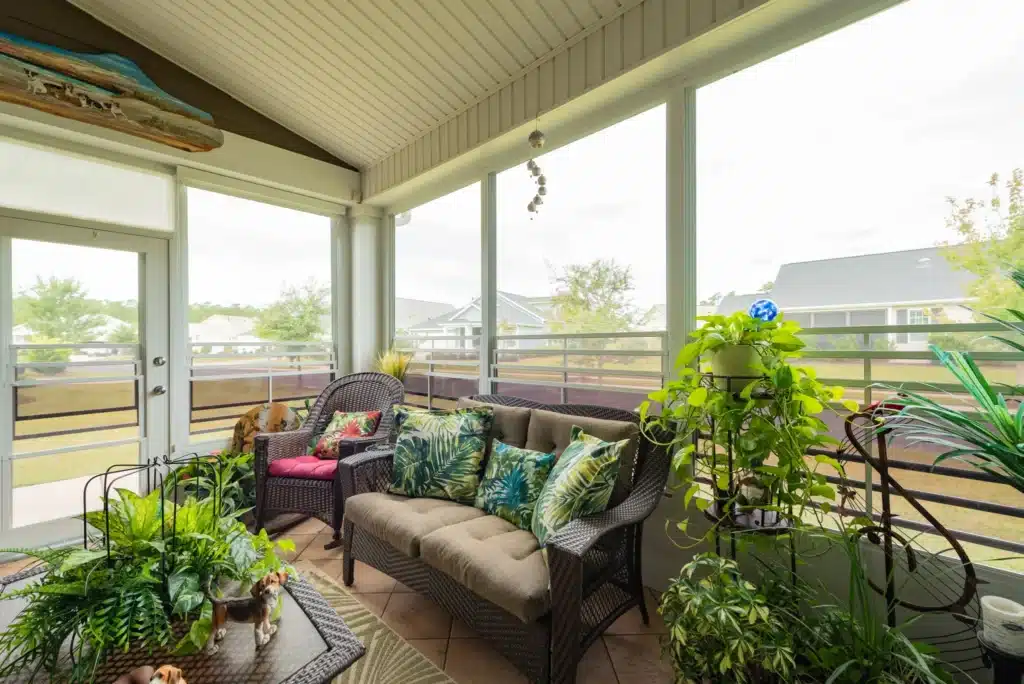 Eze-Breeze vinyl sunroom decorated with numerous houseplants, wicker furniture, and tropical-print pillows