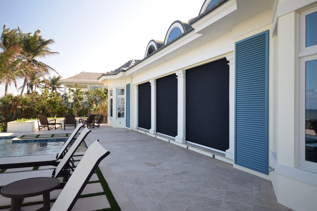 Coastal home patio with navy retractable screens lowered, blue shutters, and an ocean view