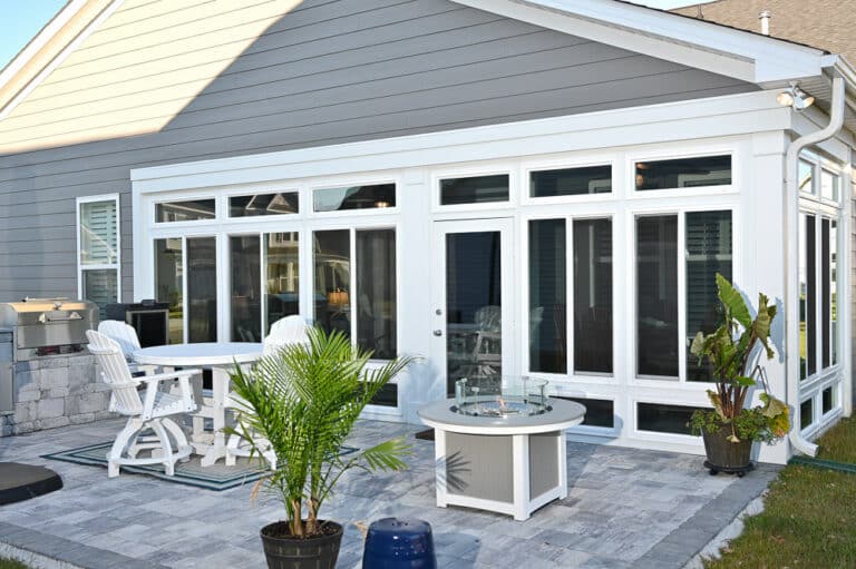 Backyard patio with a fire pit table, white adirondack chairs, and an outdoor kitchen area